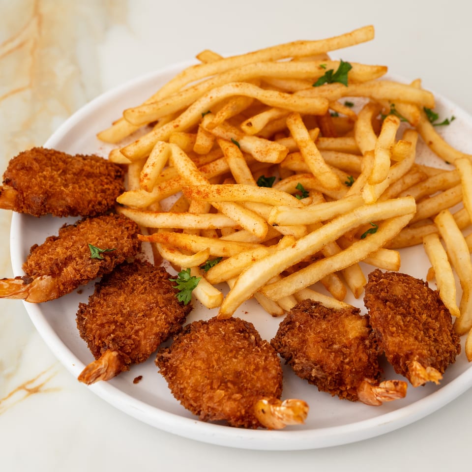 Golden fried shrimp and french fries with paprika and parsley on a white plate.