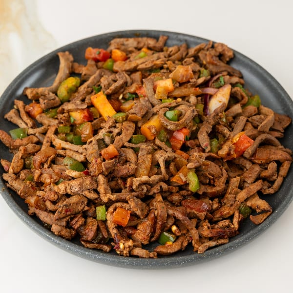 Stir-fried meat strips with colorful bell peppers and tomatoes on a dark plate.
