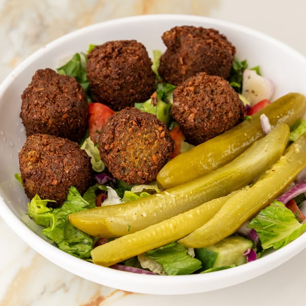 Crispy falafel, fresh green salad, and tangy pickles in a white bowl.