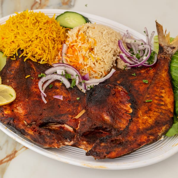 Spiced whole grilled fish with yellow and brown rice, red onion, and lemon.