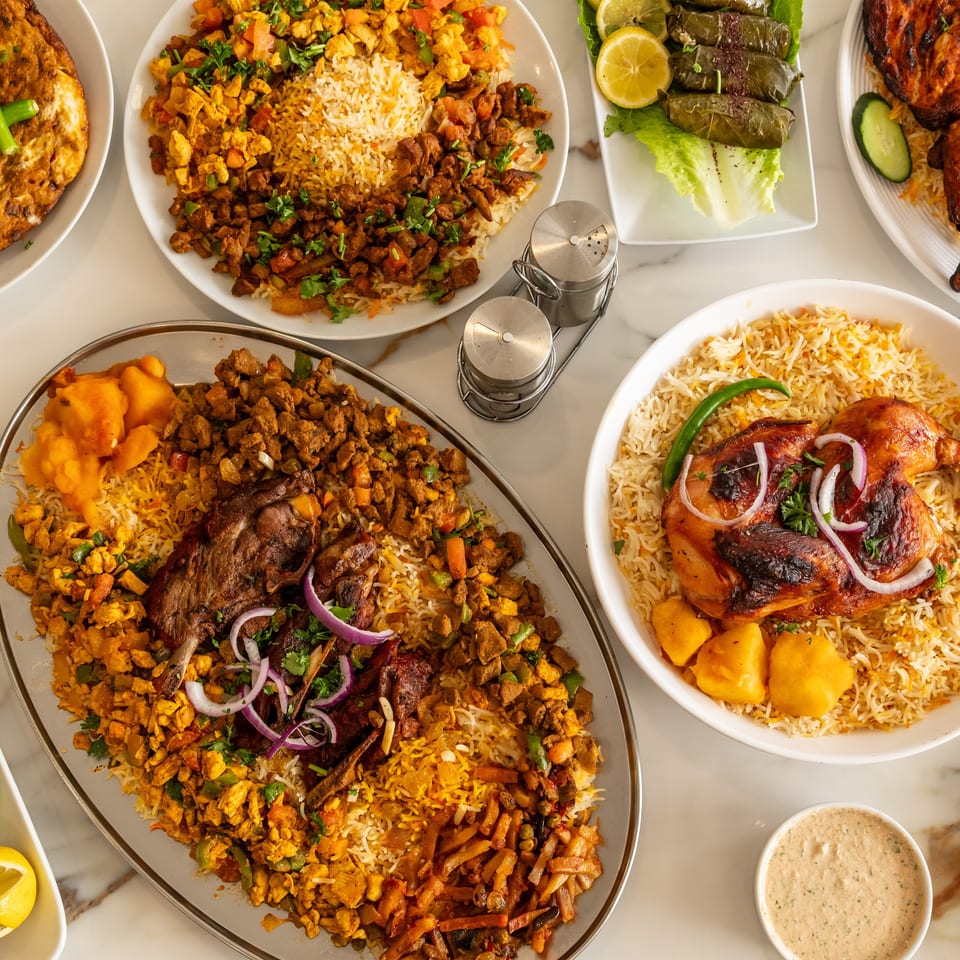 Overhead view of a large spread of Middle Eastern rice dishes with chicken, lamb, beef, and grape leaves.