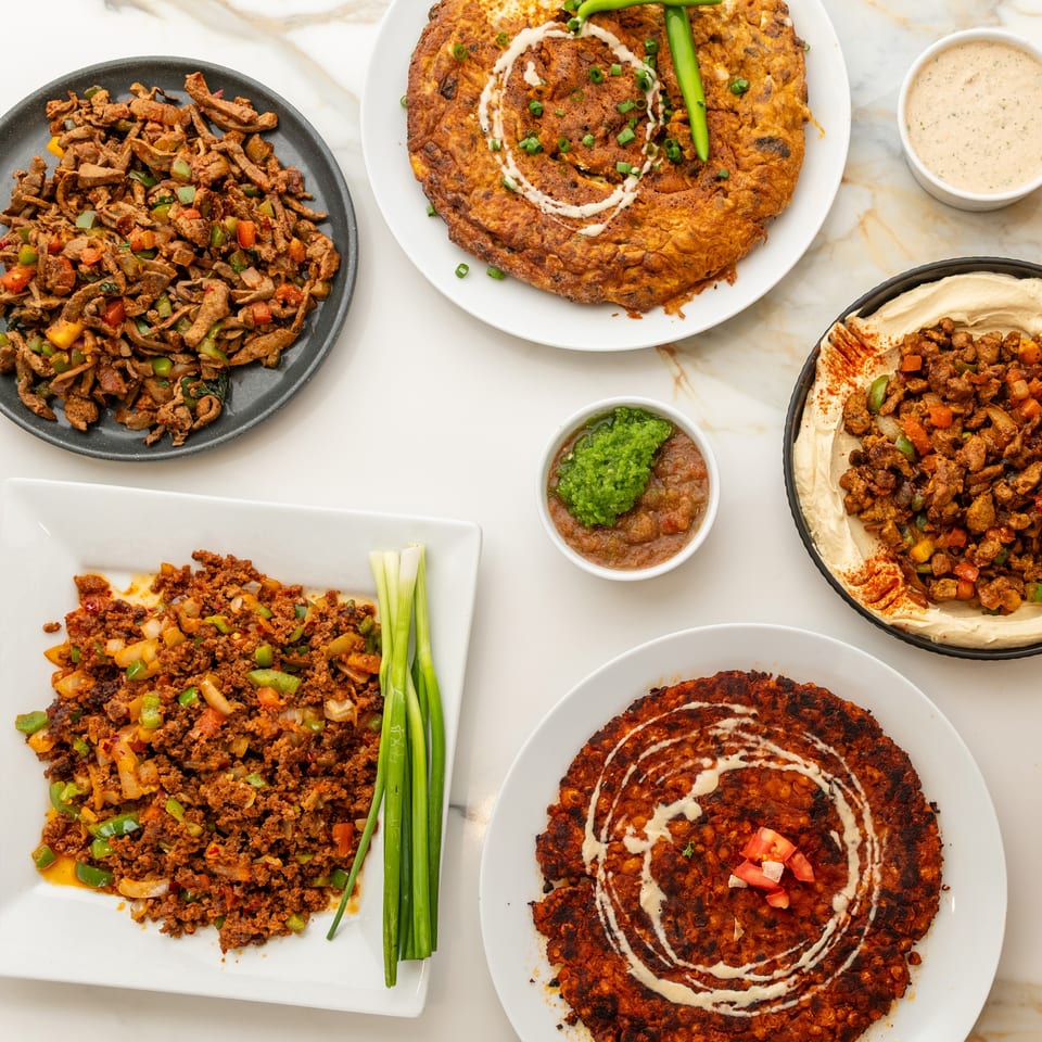 Assortment of Middle Eastern dishes on a marble table, featuring meats, hummus, and savory flatbreads.