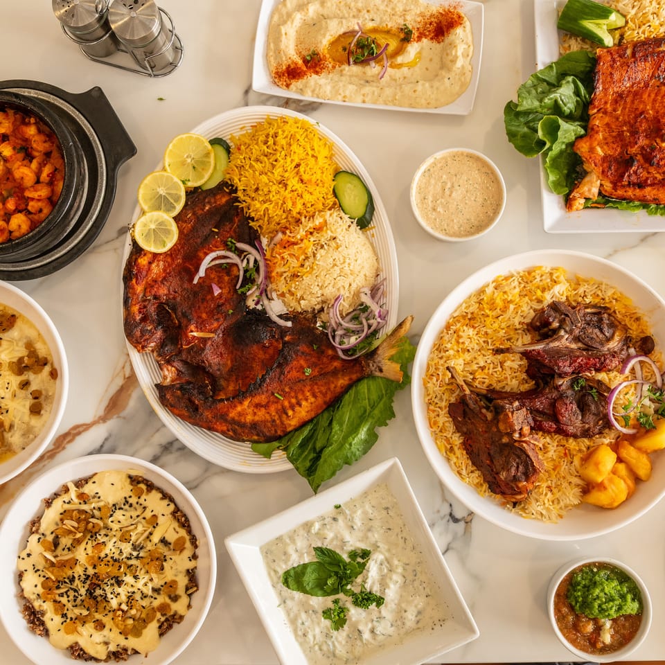 A marble table filled with various Middle Eastern dishes including grilled fish, lamb, hummus, and shrimp.