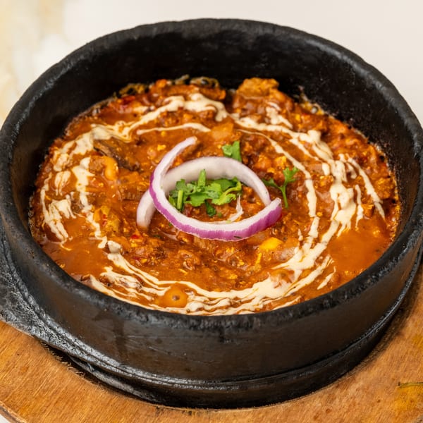 Reddish-brown curry in a black cast iron pan, garnished with cream swirls, red onion, and cilantro.