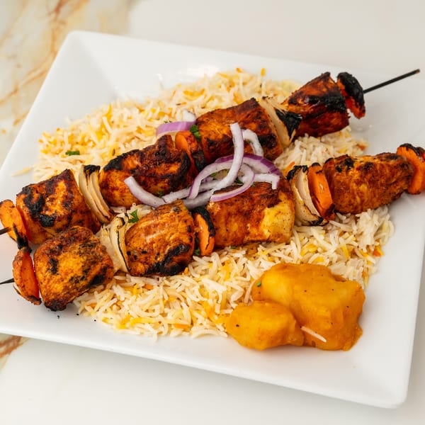 Two skewers of grilled chicken, onions, and carrots on rice, with a side of spiced potatoes.