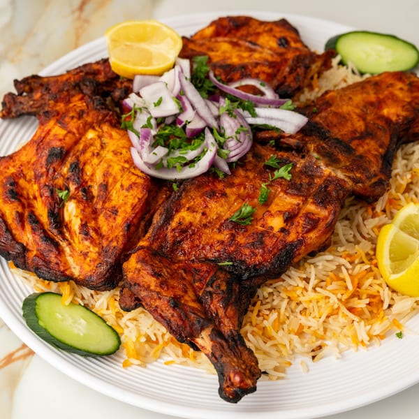 Grilled chicken and rice with red onions, parsley, lemon, and cucumber on a white plate.